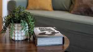 Un salon avec un canapé vert, une table basse ronde en bois, une plante en pot et un livre.