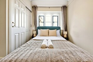 Una habitación de hotel con una cama grande, dos lámparas de noche, una ventana con cortinas y una puerta con pomo.