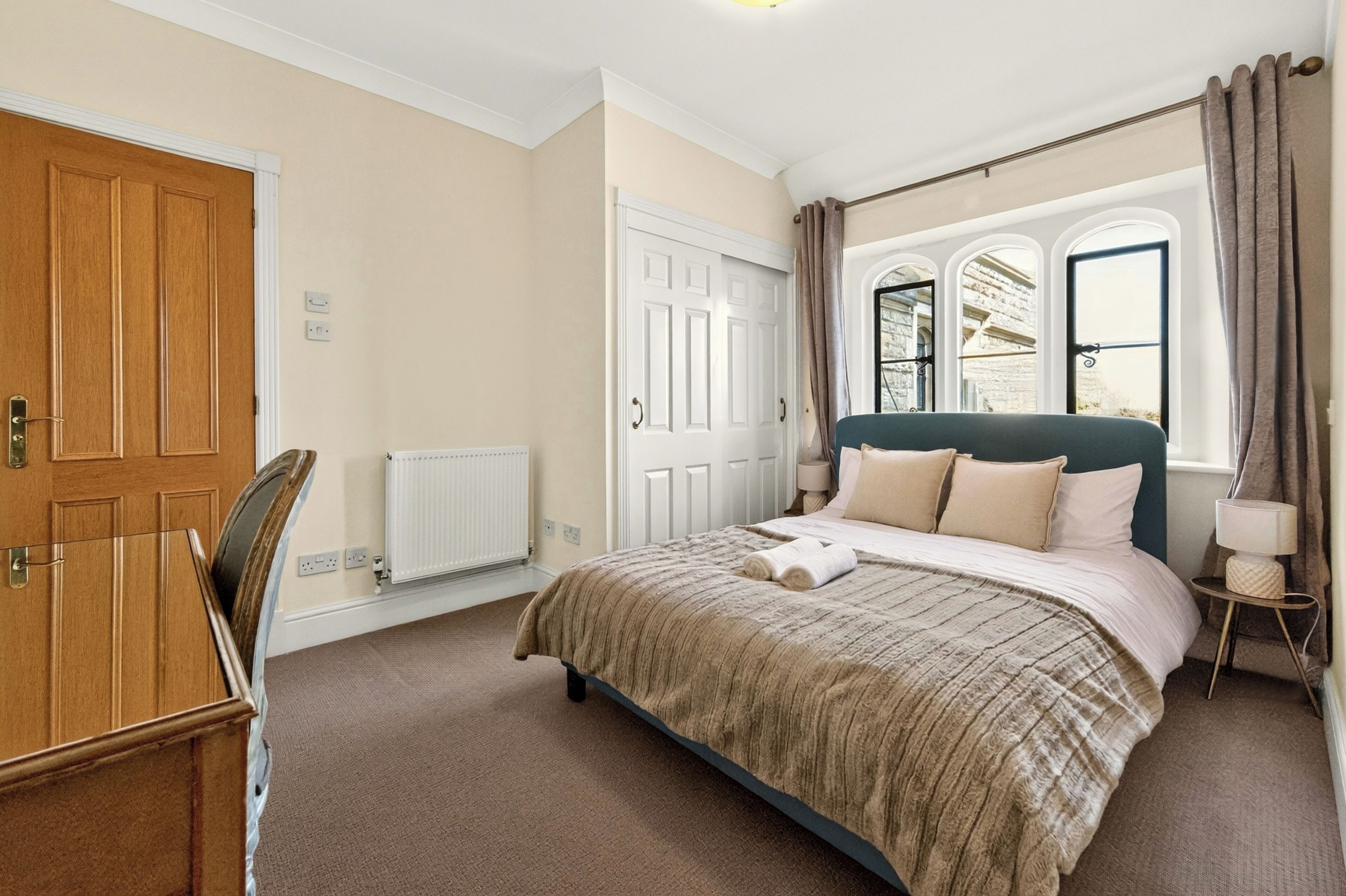 A bedroom with a large bed, a wooden wardrobe, a radiator, and a window with curtains.