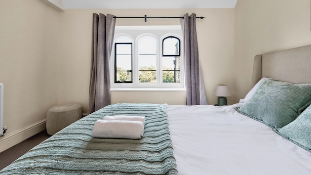 Une chambre à coucher avec un lit, une fenêtre avec des rideaux, une lampe de chevet et une vue sur l’extérieur.