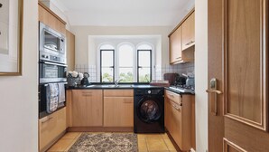 A compact kitchen with wooden cabinets, a built-in oven, a washing machine, and a window with a view.