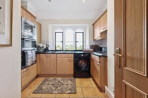 Cocina compacta con armarios de madera, horno integrado, lavadora y ventana con vistas.