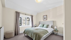 A bedroom with a bed, a window with curtains, a bedside table with a lamp, and a picture on the wall.