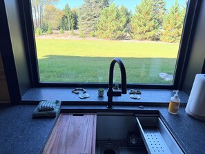 A kitchen with a window view of a grassy yard and trees.