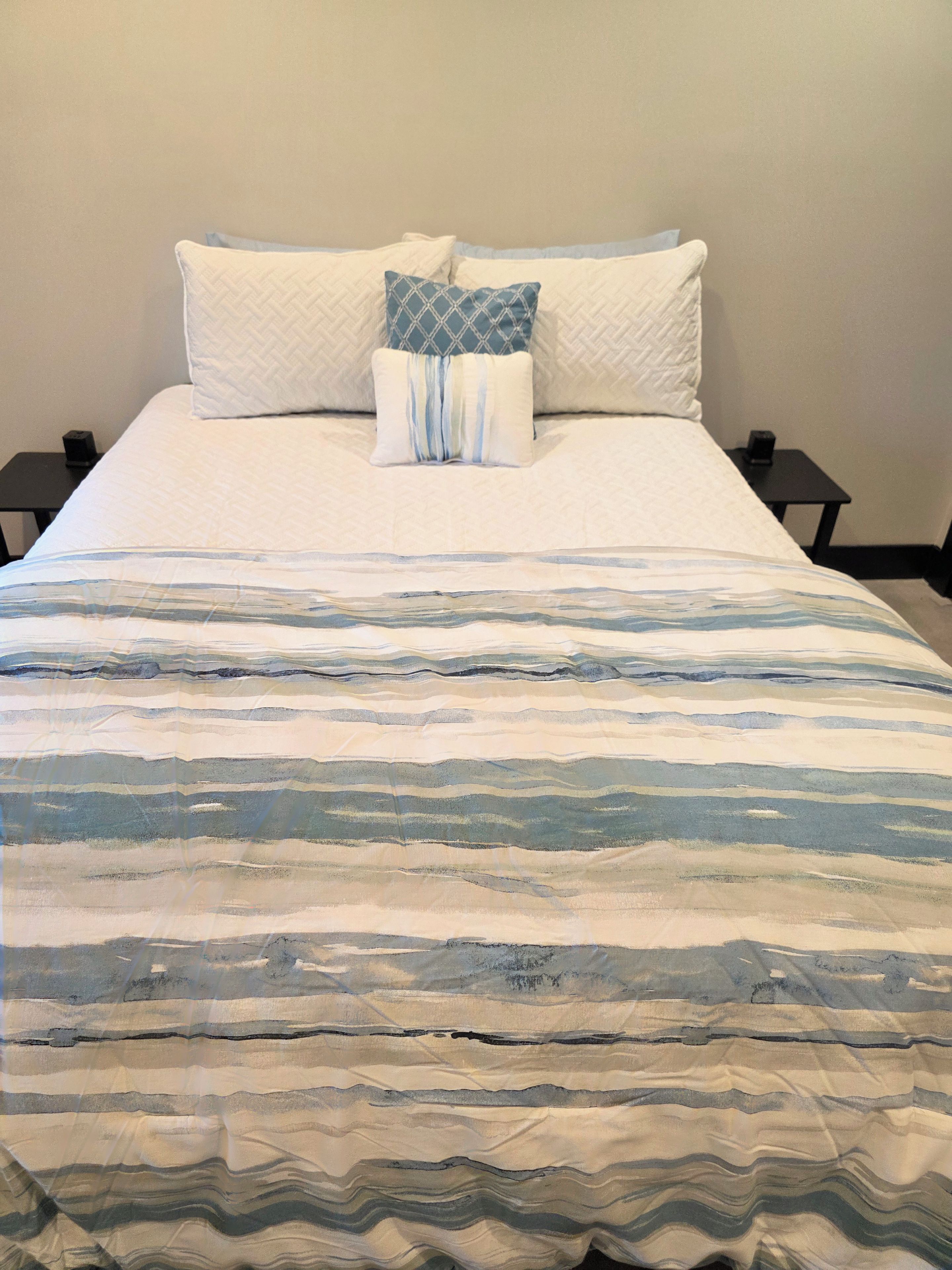 A bed with a striped bedspread, two pillows, and two bedside tables.