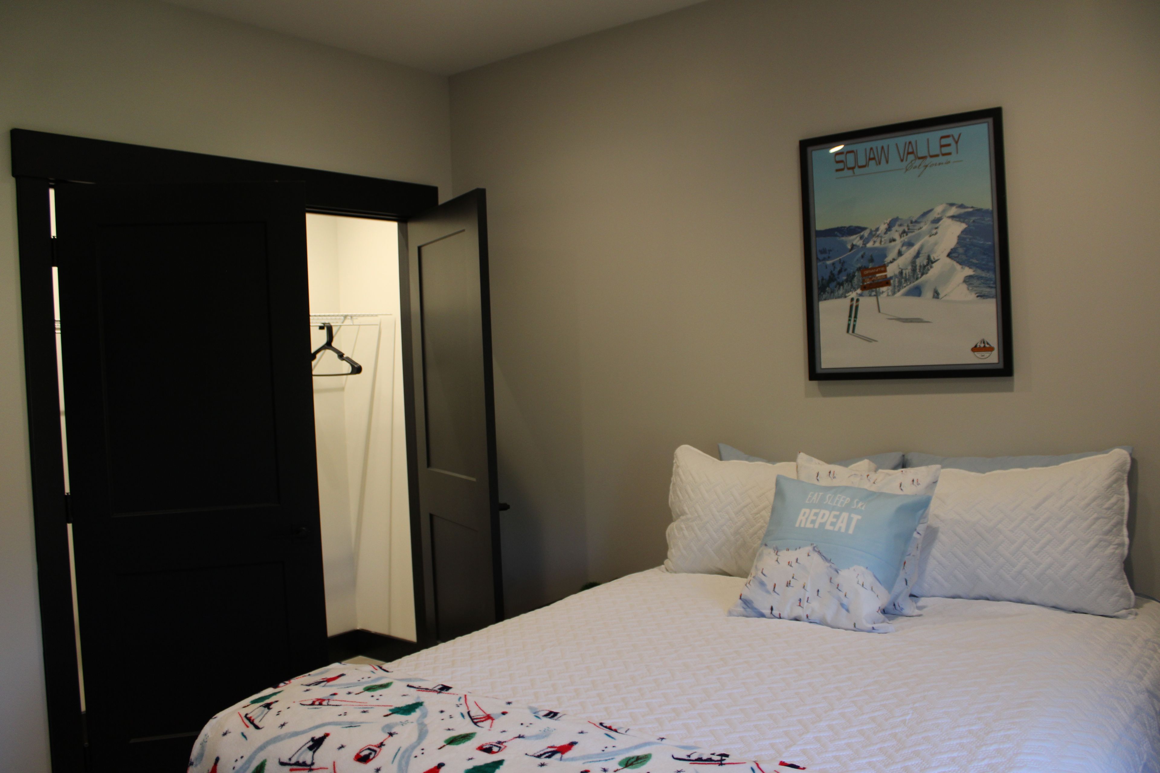 Una camera da letto con un letto, cuscini, un quadro appeso alla parete e una porta che dà su un'altra stanza.