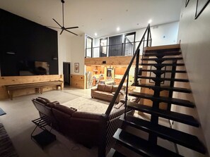Un salón amplio con un televisor de pantalla plana grande, un sofá, una mesa de centro y una escalera.