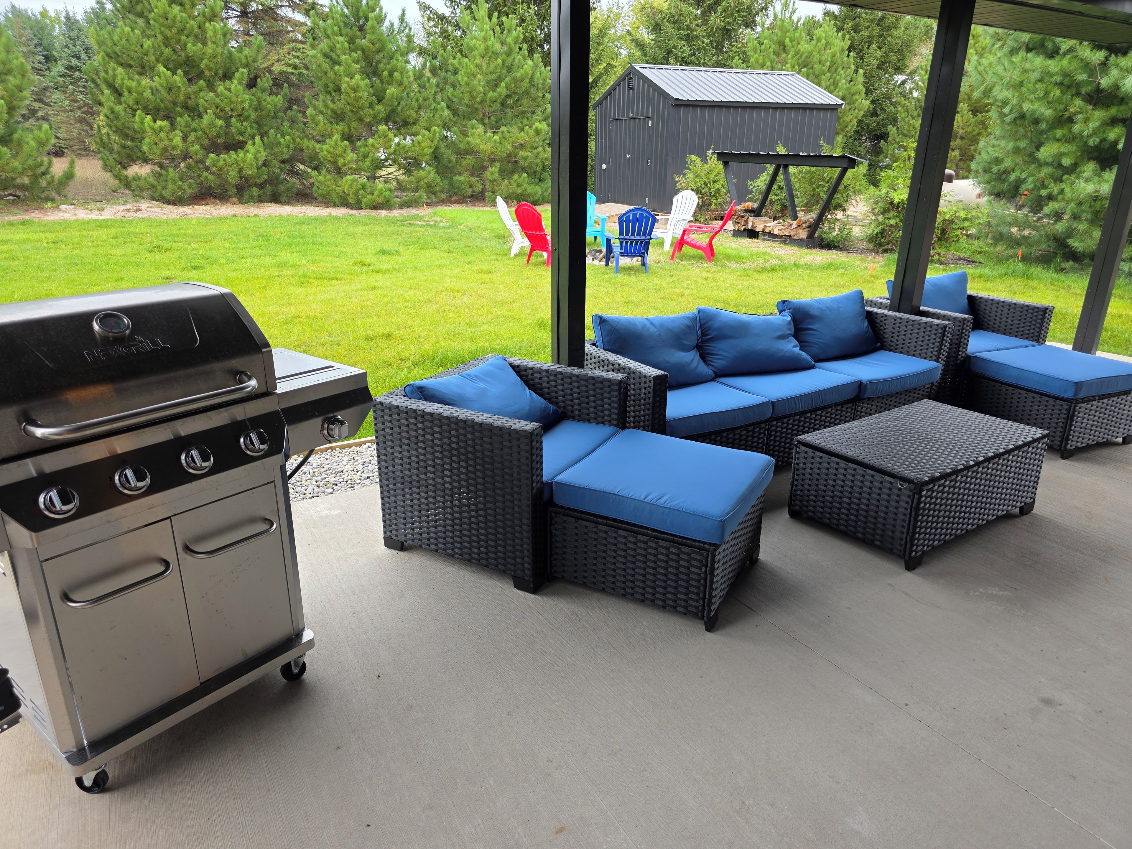 Un patio con una parrilla, muebles de exterior y vistas a un césped y árboles.