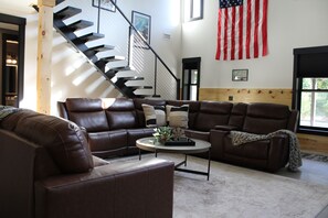 A living room with a brown leather sectional sofa, a coffee table, and a staircase with a black railing.