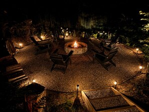 A circular outdoor seating area with a fire pit at the center, surrounded by wooden chairs and a stone fire pit.