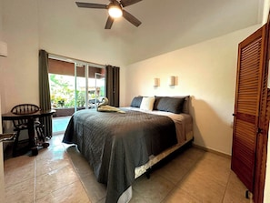 A bedroom with a bed, a desk, and a chair. There is a ceiling fan, a window with curtains, and a door. - 3-bedroom condo 1 Block from Playa La Ropa (Ixtapa Zihuatanejo)