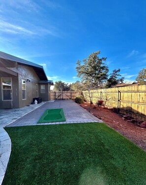 A backyard with a patio, artificial grass, a wooden fence, and a house. - Sedona Luxury 5-Bedrm Oasis, Pool-Spa, Yoga, Views (Sedona)