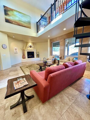 A spacious living room with a red sofa, a fireplace, and a staircase leading to an upper level. - Sedona Luxury 5-Bedrm Oasis, Pool-Spa, Yoga, Views (Sedona)