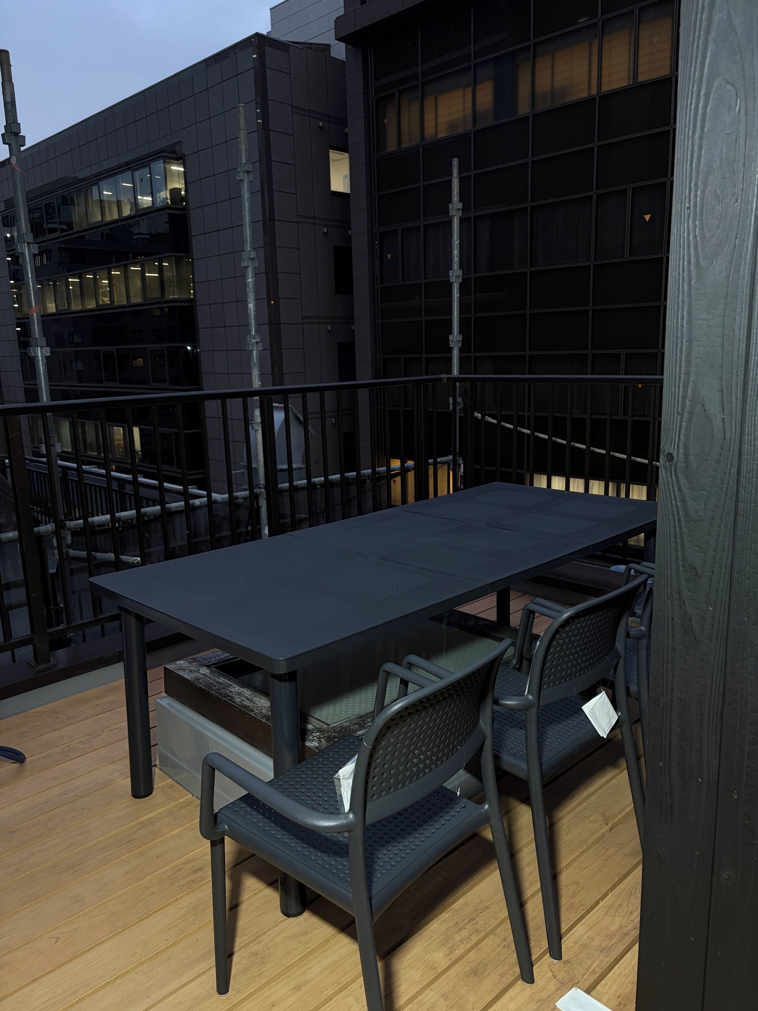 An outdoor patio with a table and chairs, a railing, and a building in the background.