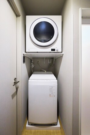 A compact laundry room with a front-loading washer and a top-loading dryer. - Hotel Matoma Annex (Minato-ku)