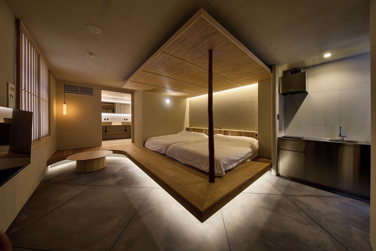 A modern bedroom with a large bed, a wooden ceiling, and a kitchenette.