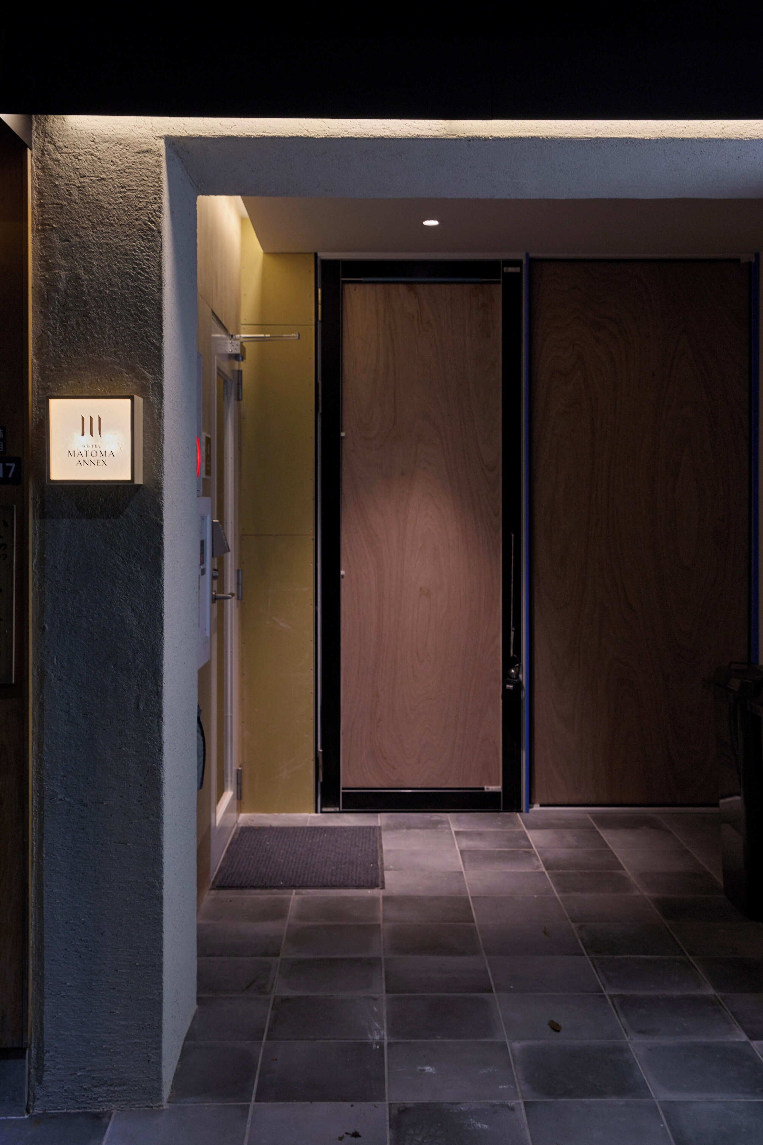 A hotel entrance with a wooden door, a reception desk, and a sign indicating the hotel name.