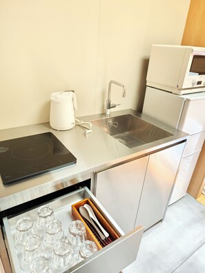 A modern kitchen with a stainless steel countertop, a built-in microwave, a kettle, and a drawer with glassware.