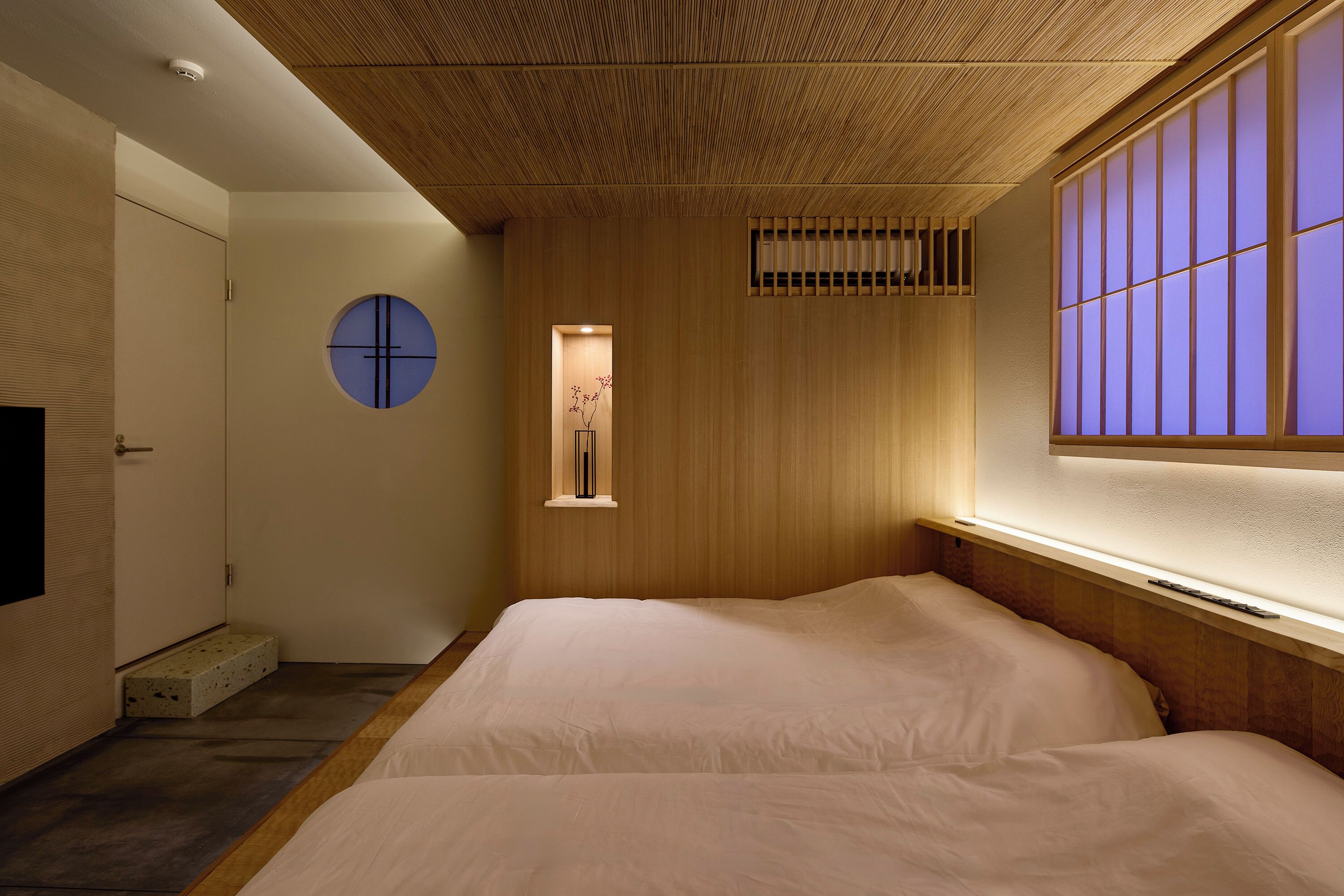 A minimalist bedroom with a large bed, a small window with a view, and a unique ceiling design.