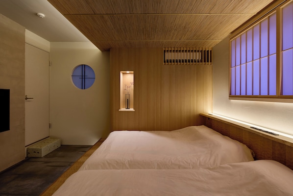 A minimalist bedroom with a large bed, a small window with a view, and a unique ceiling design.