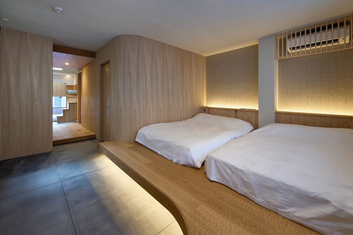A modern hotel room with two beds, a wooden floor, and a unique wall design.