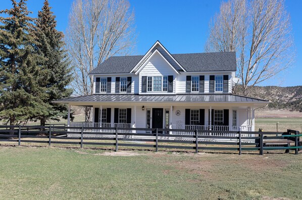 A two-story house with a porch, a fenced yard, and trees in the background.