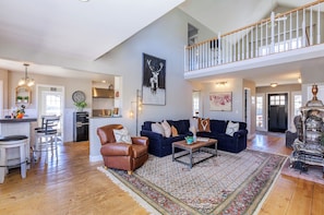 A spacious living area with a high ceiling, a dining area with a kitchen in the background, and a staircase leading to an upper level.