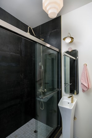 A modern bathroom with a glass-enclosed shower, a white sink, and a mirror with a towel hanging on the wall.