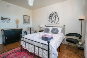 A bedroom with a bed, a dresser, a chair, a lamp, and artwork on the walls.