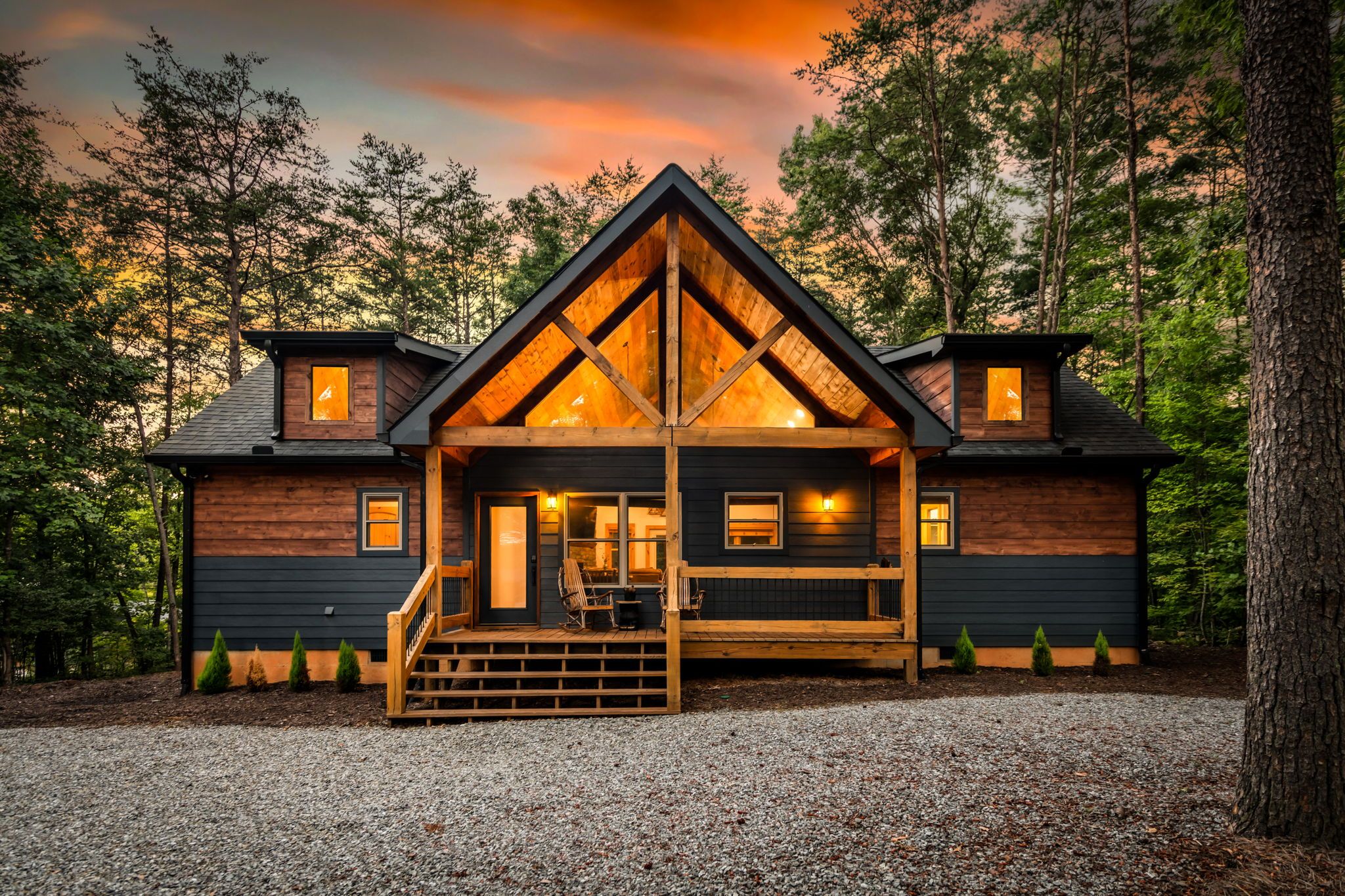 A log cabin with a prominent front porch, multiple windows, and a symmetrical roof design.