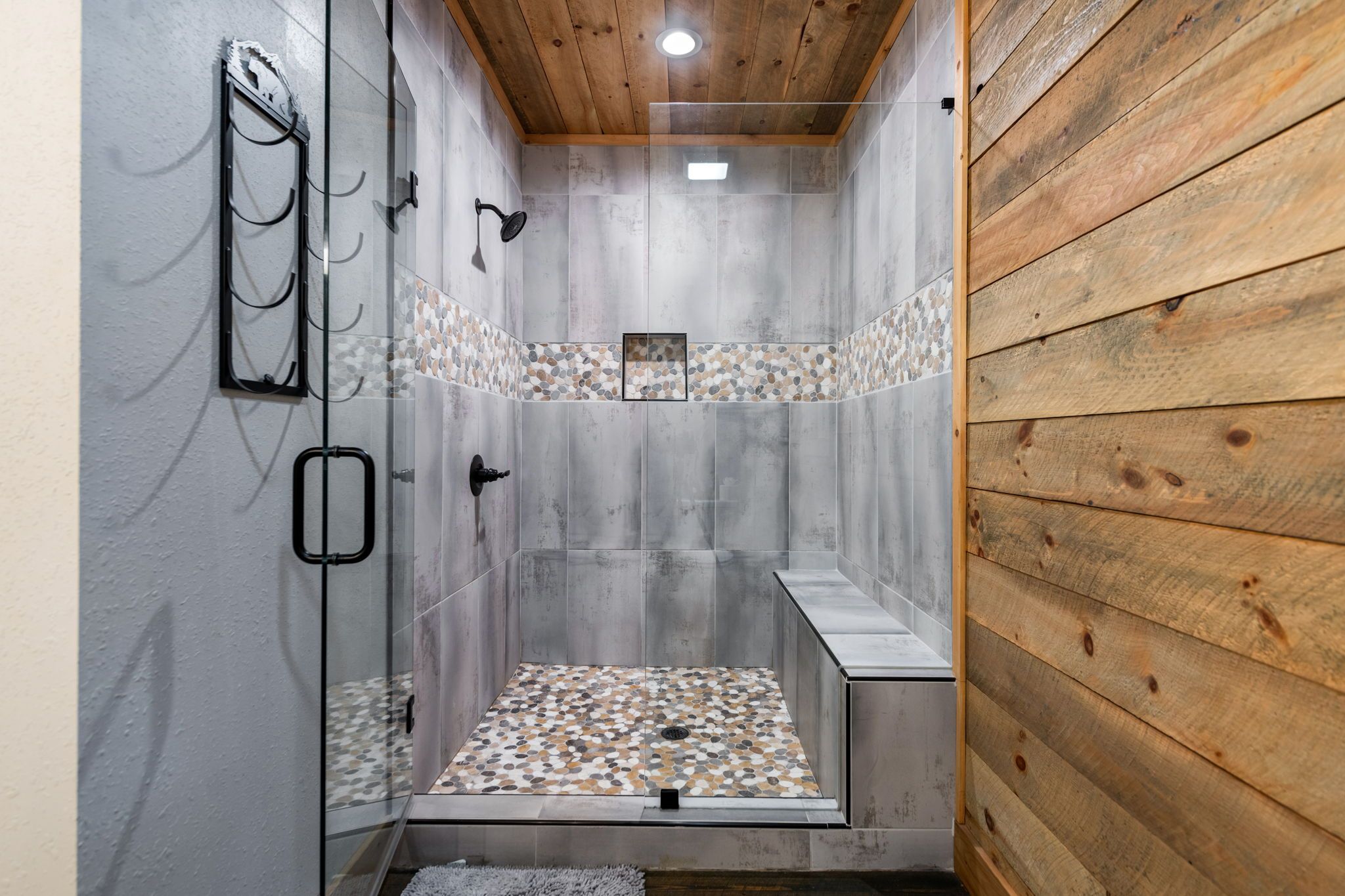 A shower with a glass door, a wooden ceiling, and a pebble-patterned floor.