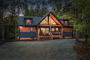 Eine Holzhütte mit markantem Satteldach, einer Veranda mit Holzbalkon und einer Auffahrt mit Kiesbefestigung.