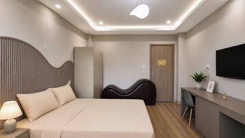 Habitación de hotel moderna con cama, mesita de noche, lámpara, armario, escritorio, silla, televisor y una planta en maceta.