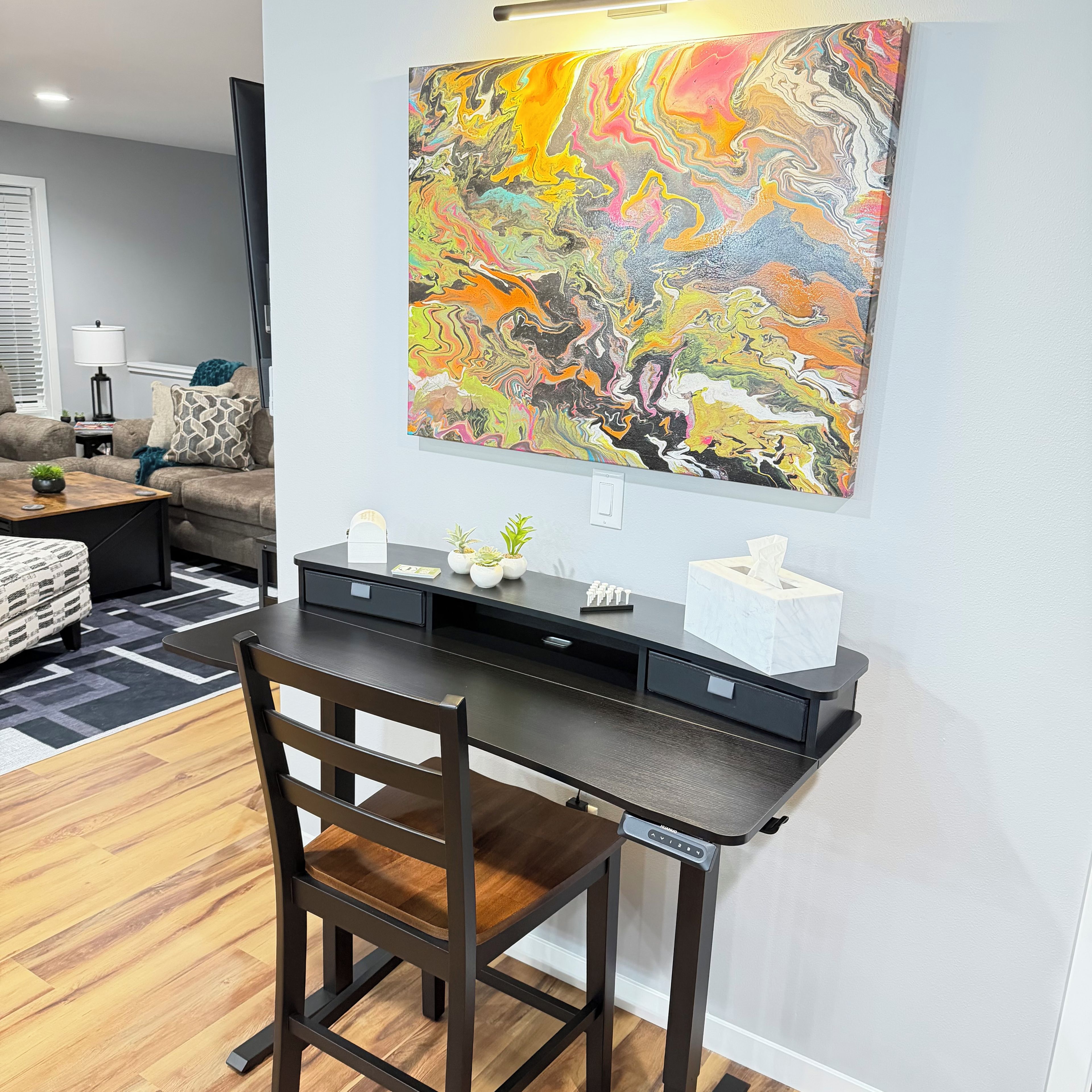 A modern home office with a desk, chair, and a colorful abstract painting on the wall.