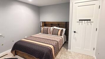 A bedroom with a bed, a ceiling fan, a door, and a carpeted floor.