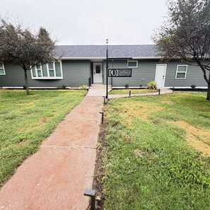 Una propiedad residencial con entrada principal, un camino que lleva a la puerta y un letrero que indica el nombre y la dirección del inmueble.