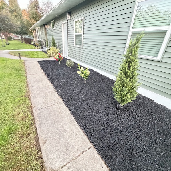 A residential property with a landscaped garden bed, a pathway, and a house with a siding exterior.