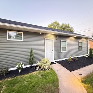 A single-story building with a front door, two windows, and a small garden area with various plants and flowers.