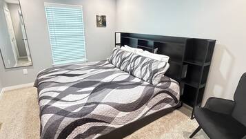 A bedroom with a bed, a ceiling fan, a window with blinds, a black chair, and a black headboard.
