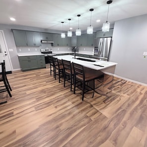 A modern kitchen with grey cabinets, a stainless steel refrigerator, and a wooden dining table with chairs.