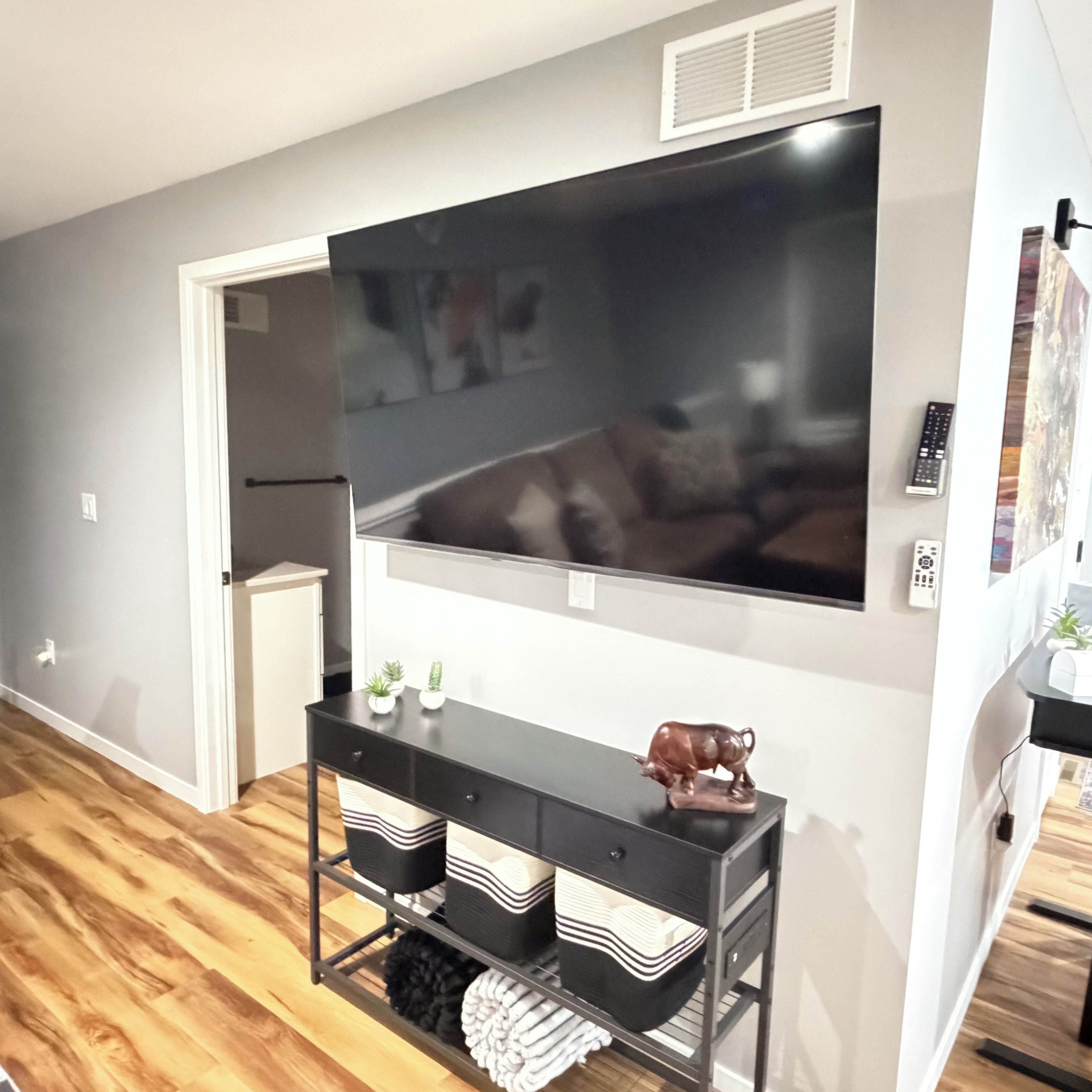 Un salon doté d’un grand téléviseur à écran plat fixé au mur, d’une console noire agrémentée d’objets décoratifs et d’un plancher en bois.