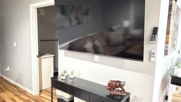 Un salon doté d’un grand téléviseur à écran plat fixé au mur, d’une console noire agrémentée d’objets décoratifs et d’un plancher en bois.