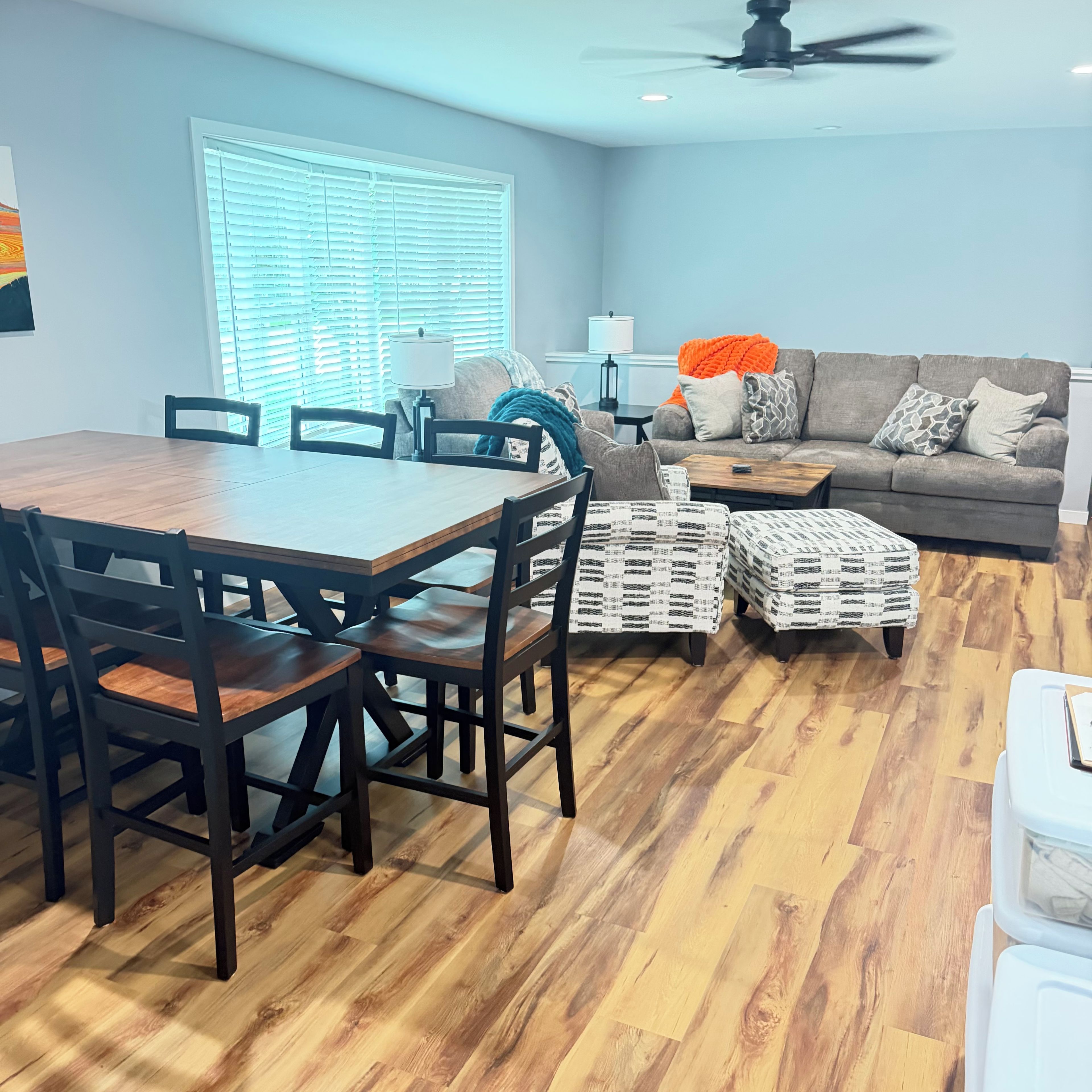 A dining area with a wooden table and chairs, a sofa with patterned cushions, and a ceiling fan.