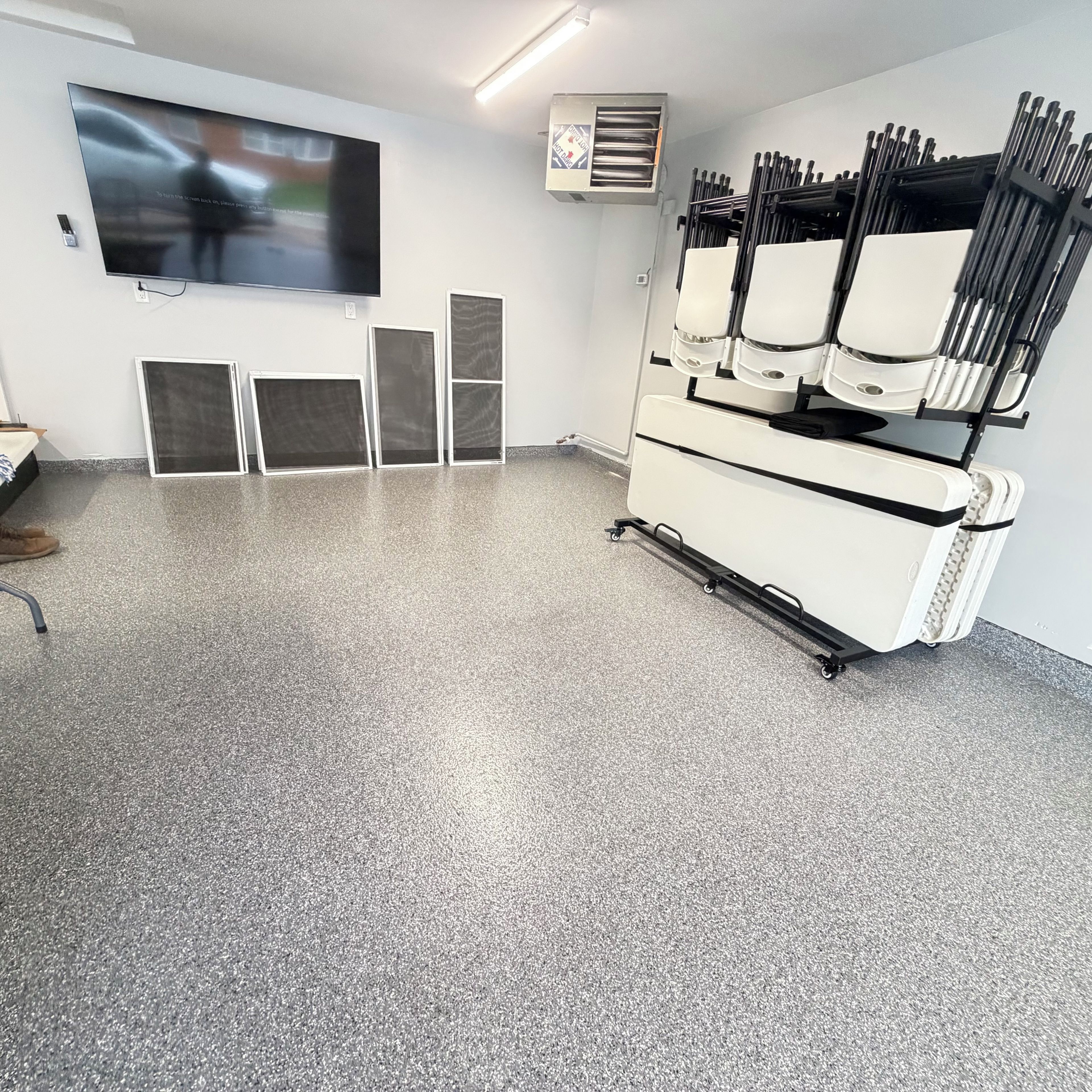 A clinical room with a large screen, a white cabinet with drawers, and a speckled floor.