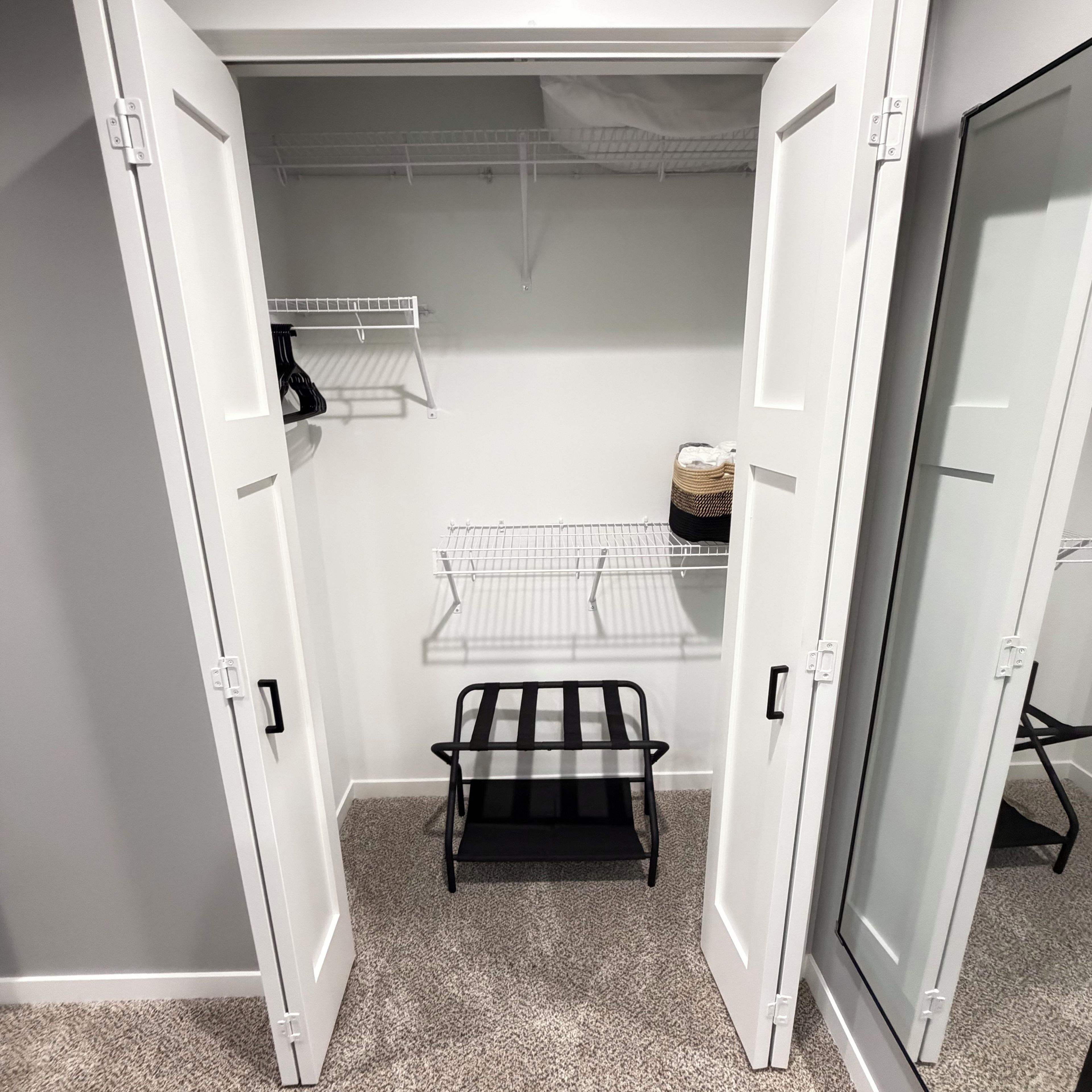 A walk-in closet with open doors, featuring a metal rack, a black chair, and a hanging storage unit.