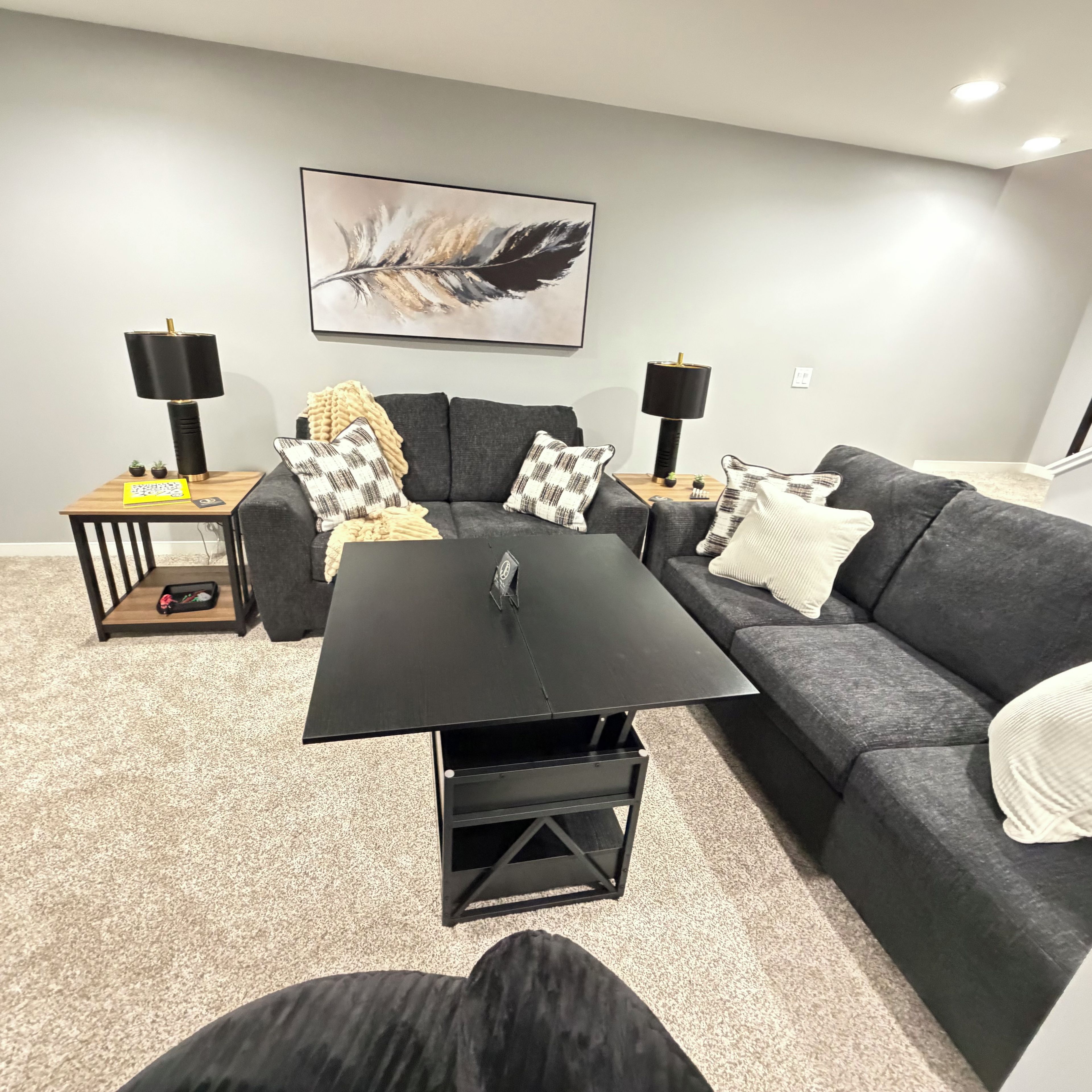 Un salon moderne avec un canapé gris, une table basse noire et deux petites tables d’appoint avec des lampes.