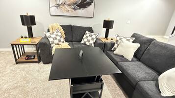 A modern living room with a grey sofa, a black coffee table, and two side tables with lamps.