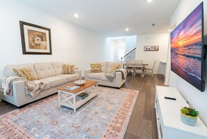 A modern living room with two sofas, a coffee table, a rug, and a large TV screen. - Pool Jacuzzi | Gated community | 6 Min to Beach (Palm Coast)