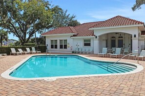 A swimming pool with a tiled deck, lounge chairs, and a building with a red-tiled roof.