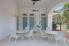 A covered patio with white walls, blue doors, and a ceiling fan. There are multiple tables and chairs arranged for outdoor dining. - Pool Jacuzzi | Gated community | 6 Min to Beach (Palm Coast)